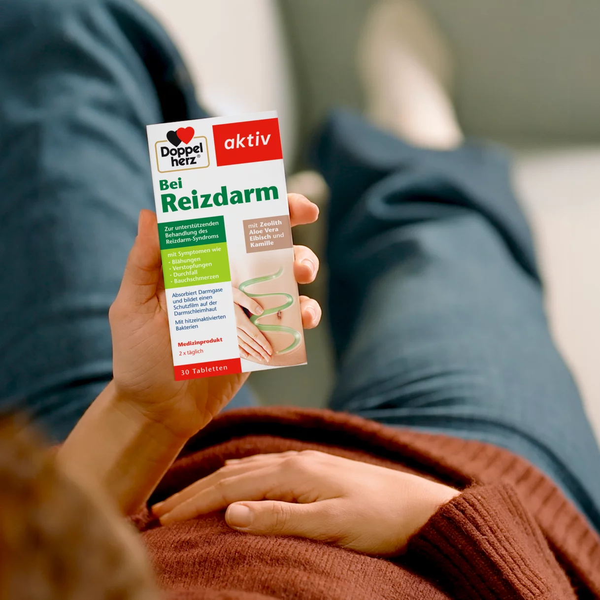 Mann hält sich den Bauch und hält Doppelherz Bei Reizdarm in der anderen Hand